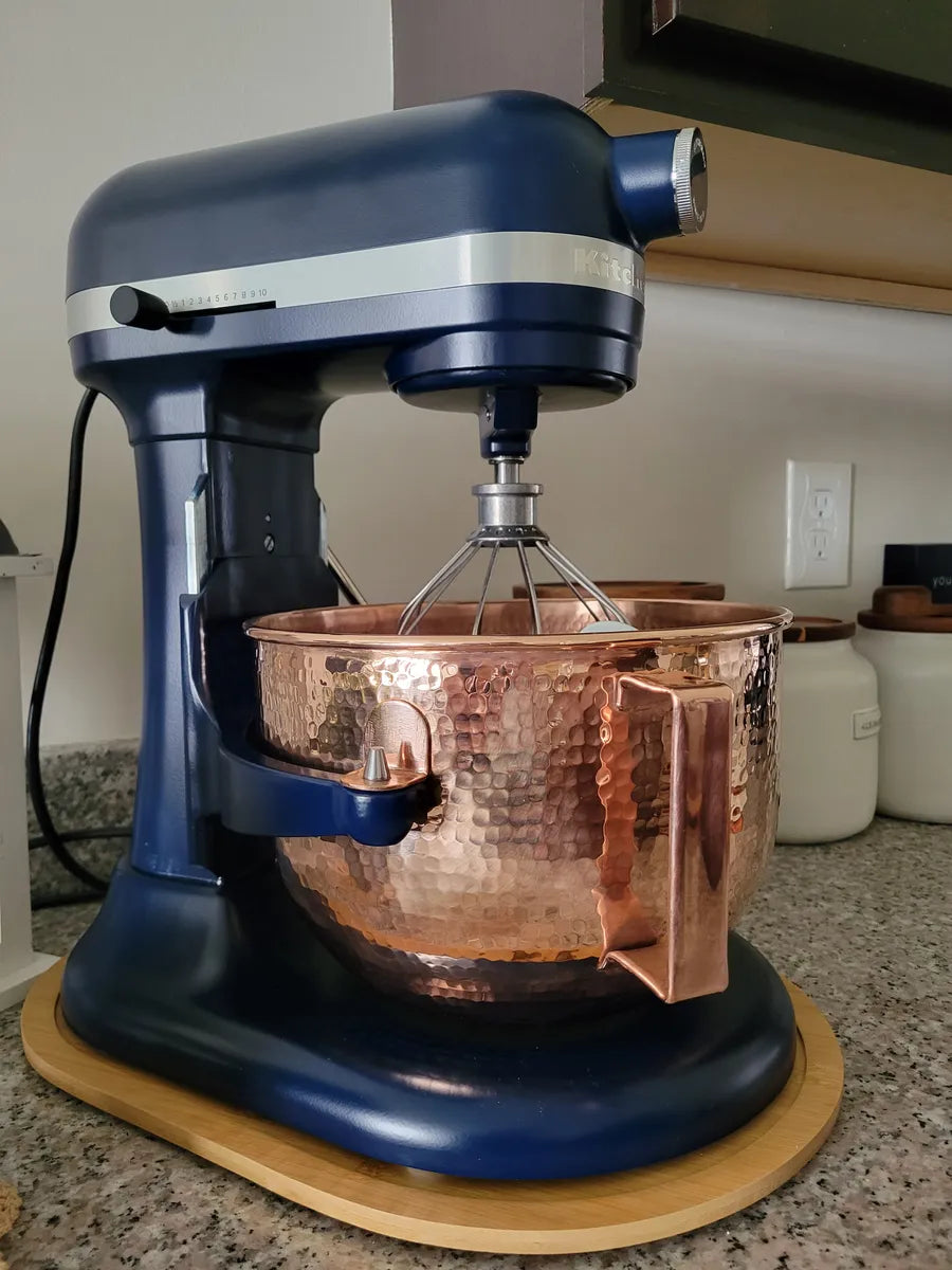 Hand-hammered copper mixing bowl attached to a navy blue KitchenAid lift stand mixer for a stylish, professional kitchen.
