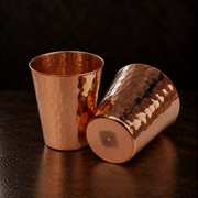 Two 2.5oz solid copper shot cups with a hammered finish, elegant design, and durable, heavy-gauge construction.