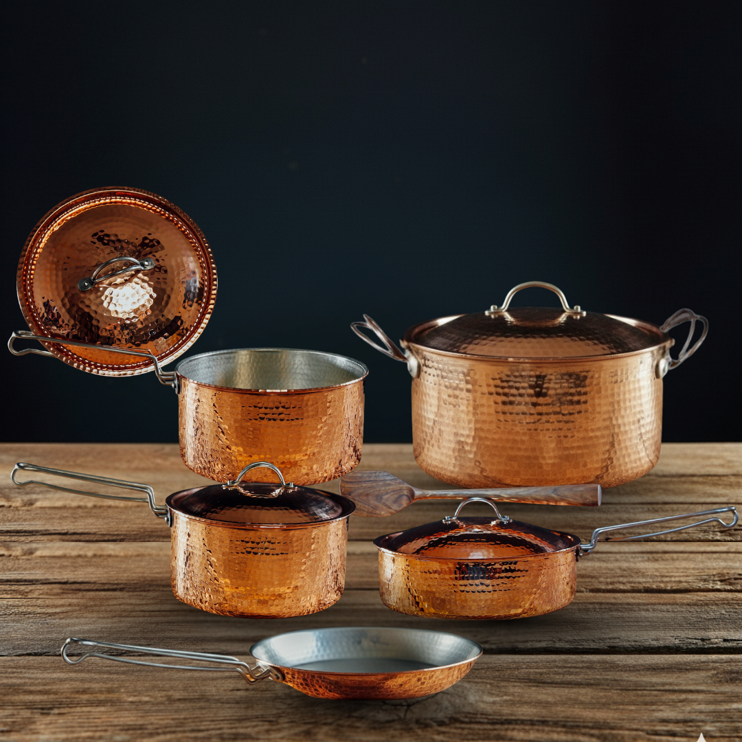 5-piece hammered copper cookware set with tin interiors, including pots, skillet, and Dutch oven on wood.