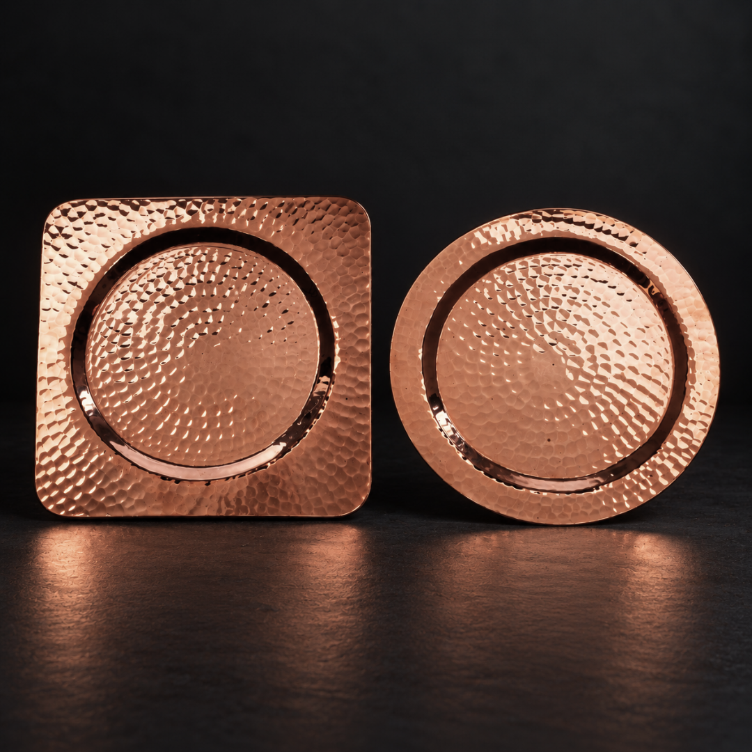 Hand-hammered 4.5-inch square and round recycled copper coasters with a warm, elegant finish on a dark surface.