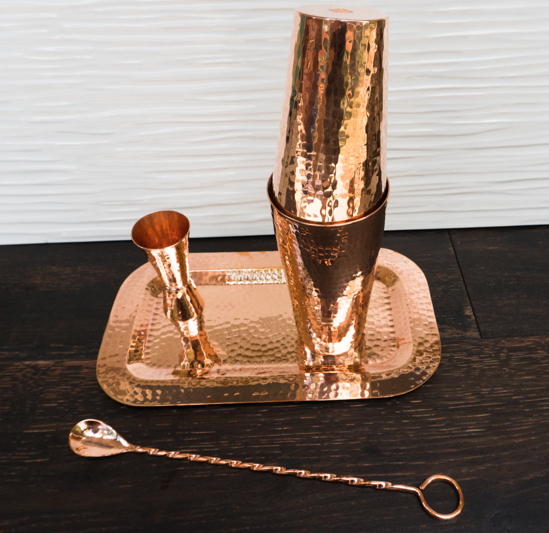 Hammered copper barman's set: shaker, jigger, twisted bar spoon, and rectangular serving tray.