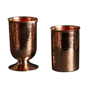 Two hammered copper cocktail glasses: one rounded with a pedestal base, one flat-bottomed.