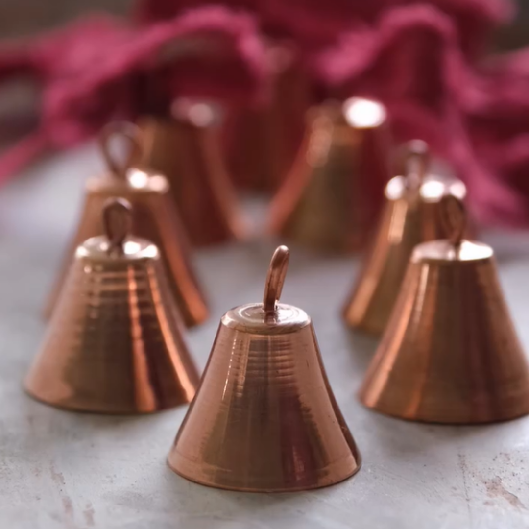 A cluster of small, hammered copper mantra bells with a rich, reddish hue.