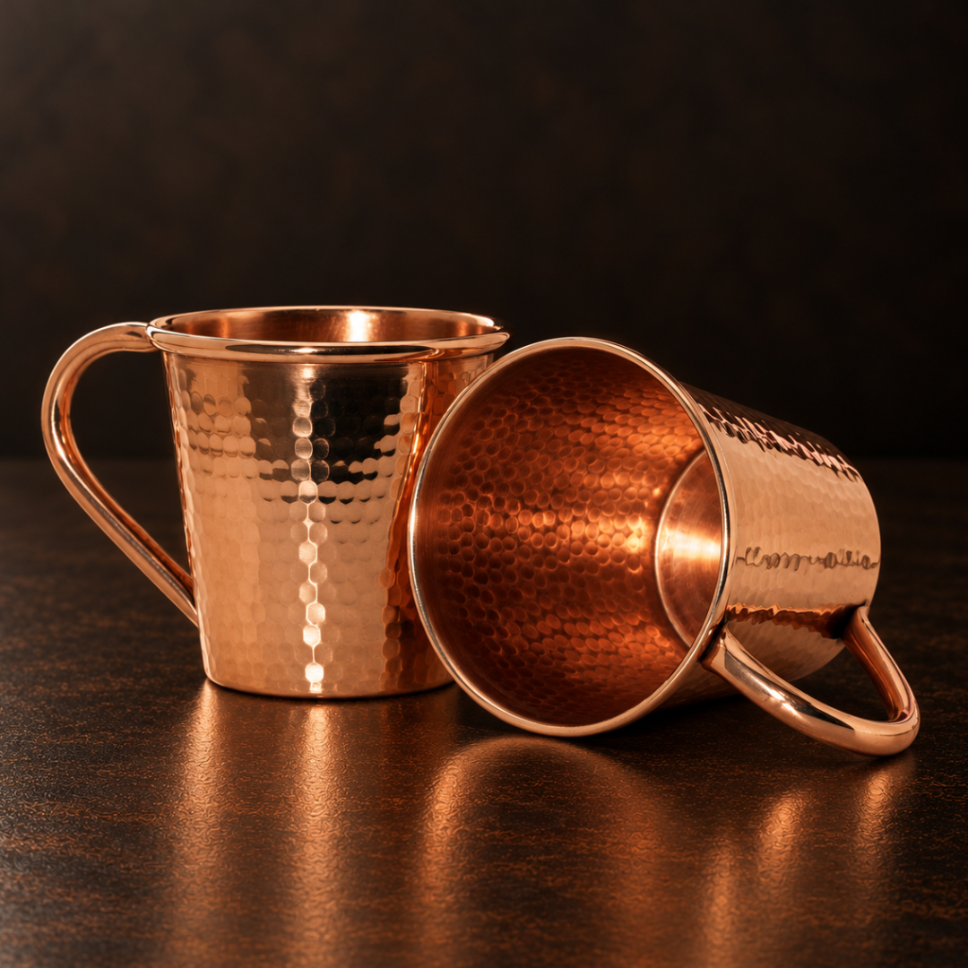 Two 12oz hammered solid copper Moscow Mule mugs with durable copper handles on a dark surface.