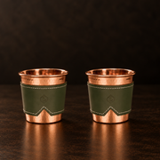 Two 12-oz hammered copper cups with olive green stitched leather sleeves featuring an anchor logo.