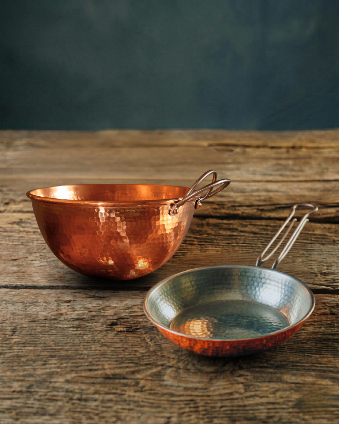 Hand-hammered copper 10" mixing bowl and skillet set on a rustic wooden surface.