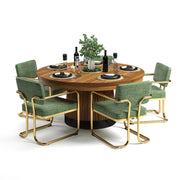 Round wooden dining table with a fluted base, set with black dishes, wine, and a plant, surrounded by six green and gold chairs.