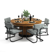 Round wooden dining table with fluted base, set with black dishes, wine, and six gray upholstered chairs.
