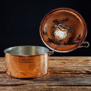 Hammered copper saucepan with lid and ergonomic handle, 1.5 quart, on a wooden surface.