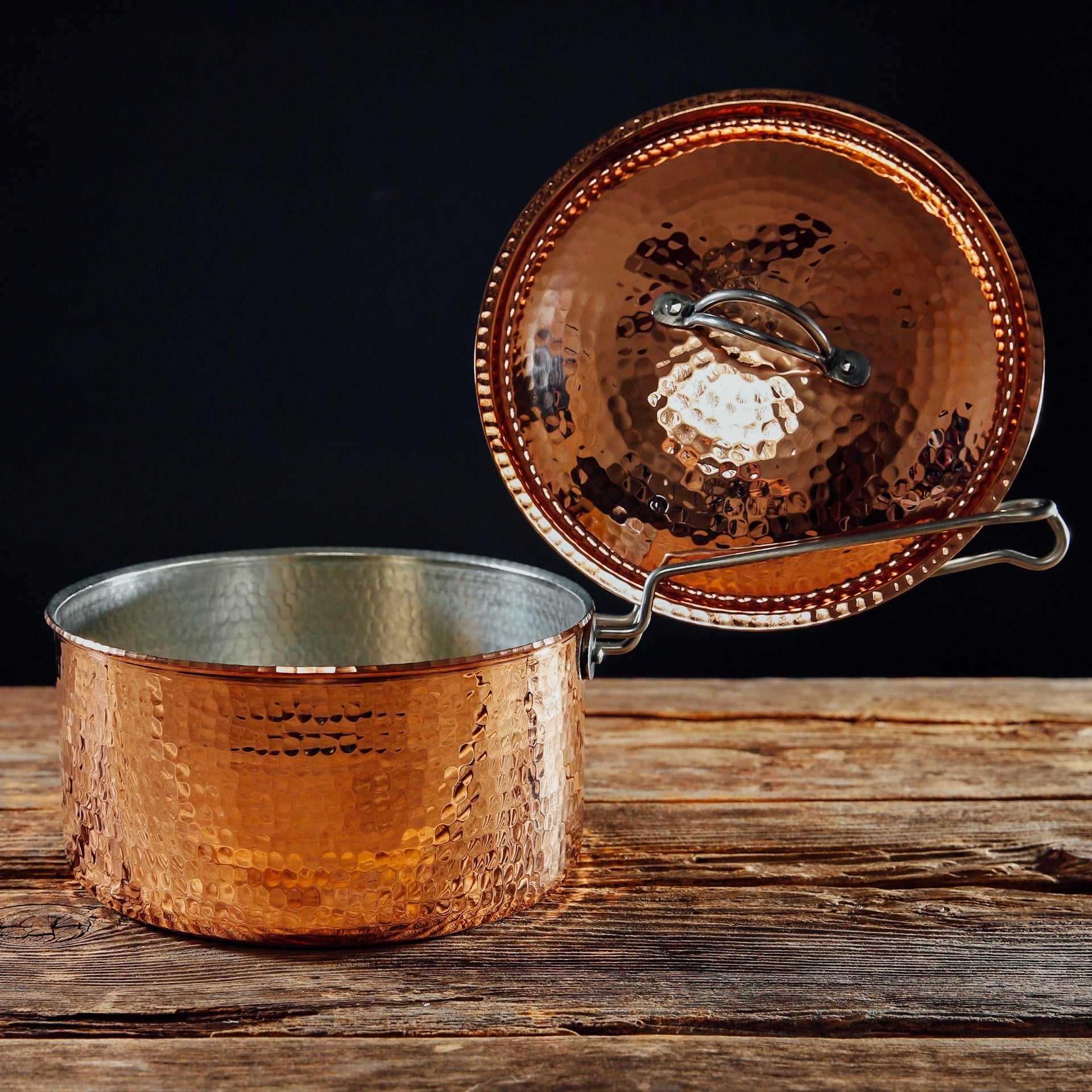 Hammered copper saucepan with lid and ergonomic handle, 1.5 quart, on a wooden surface.