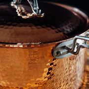 Close-up of a hammered copper saucepan with a matching lid and silver handle.