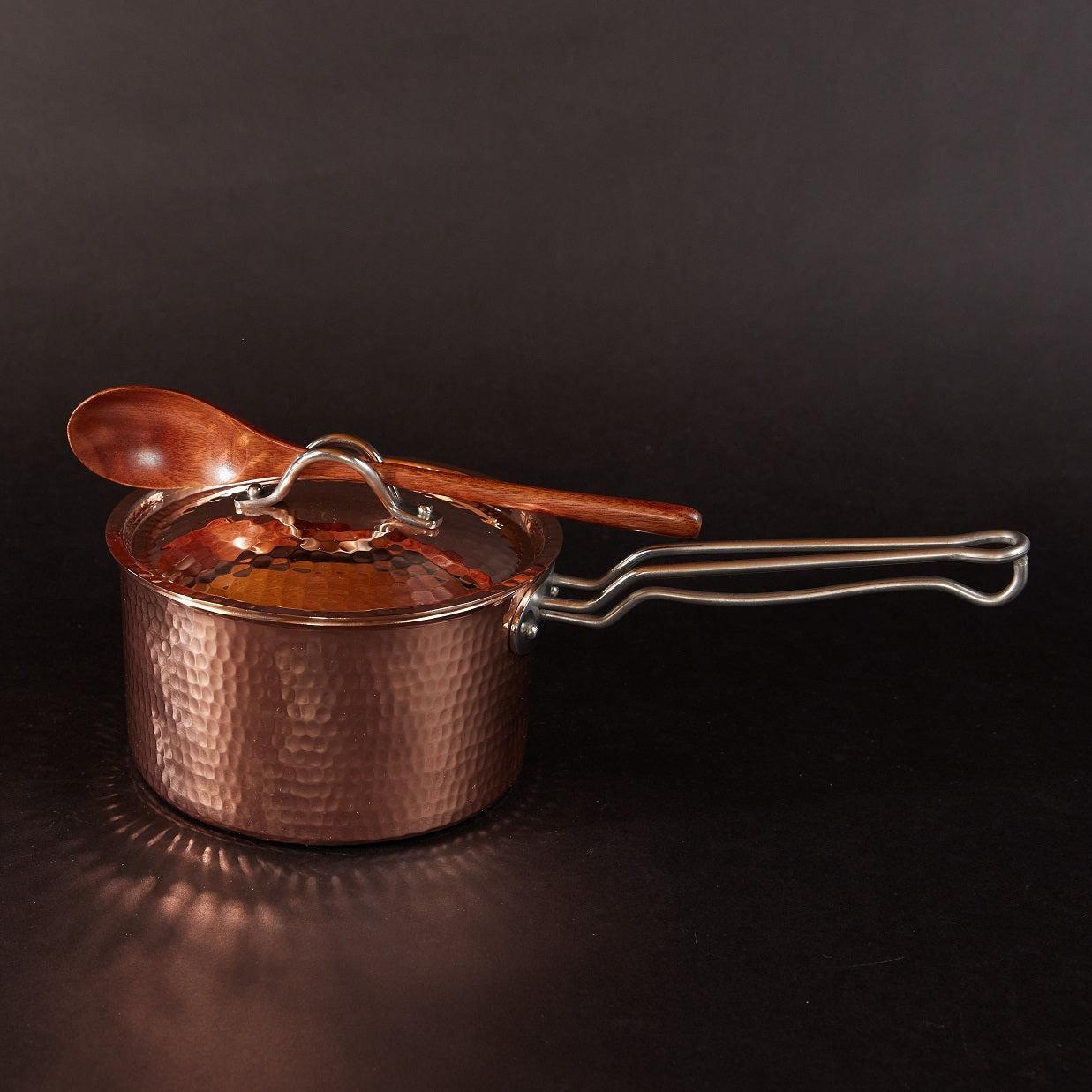 Hammered copper 1.5 quart saucepan with lid, ergonomic handle, and wooden spoon resting on top.