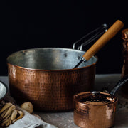 Two hammered copper saucepans, a large 2.5 quart with a wooden handle and a small 1.5 quart with a lid.