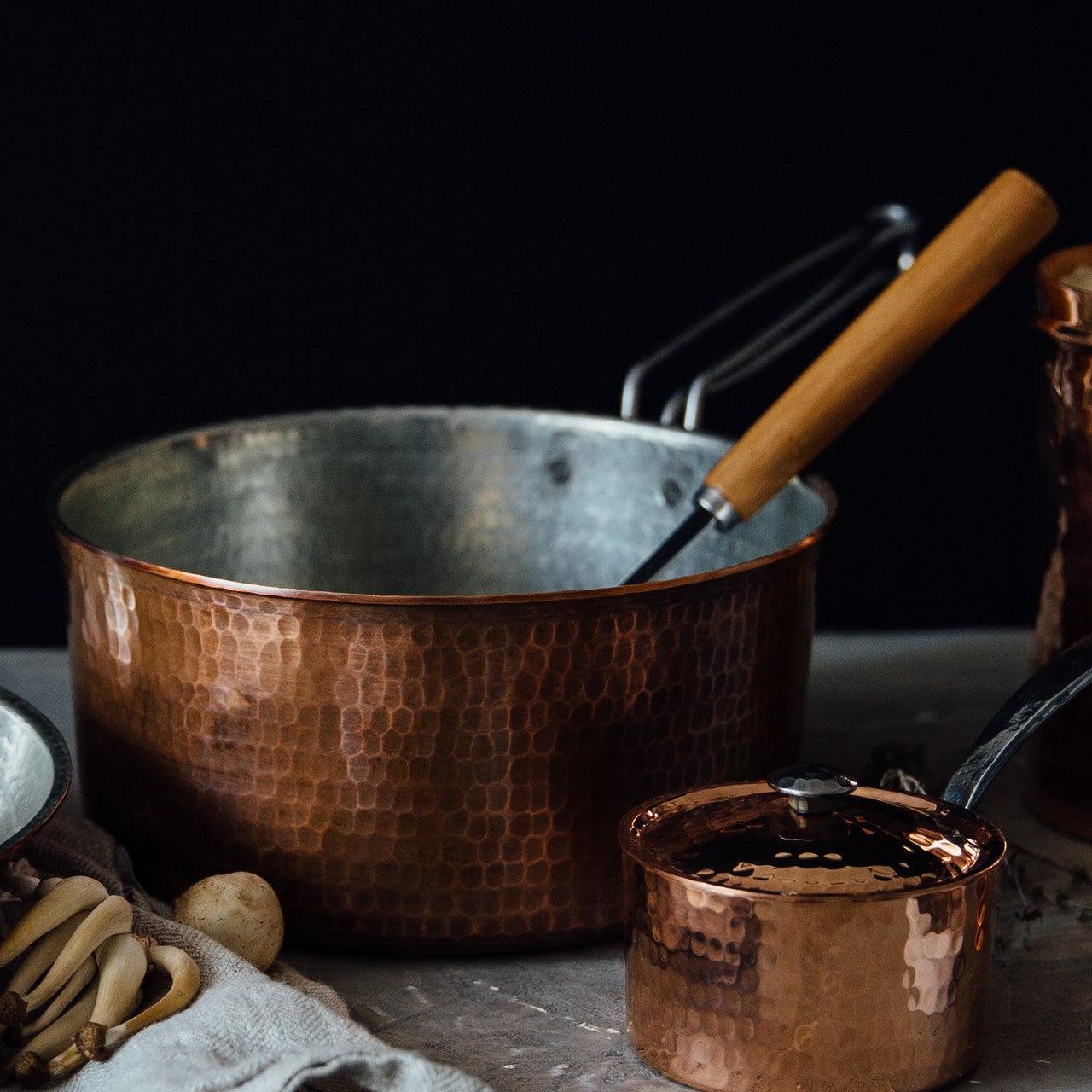 Two hammered copper saucepans, a large 2.5 quart with a wooden handle and a small 1.5 quart with a lid.