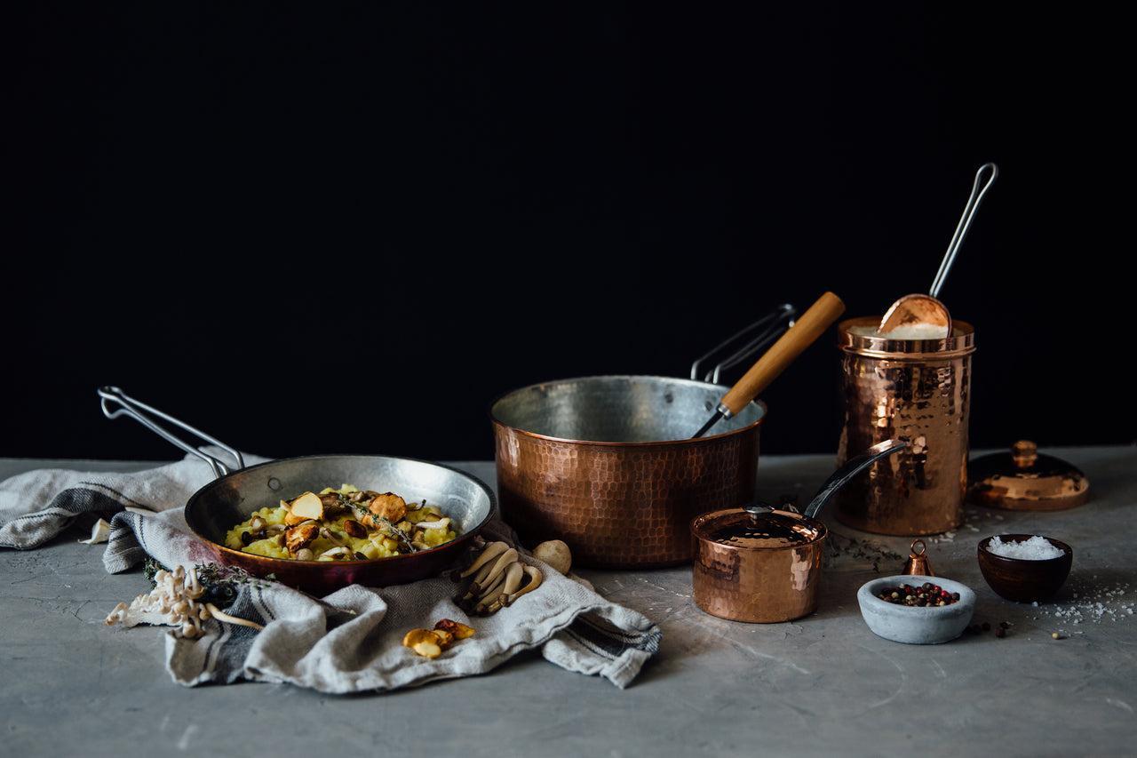 Hammered copper saucepan set with a frying pan, small pot, and storage canister on a gray counter.