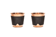 Two 12 oz hammered copper mugs with black leather sleeves featuring a subtle logo.