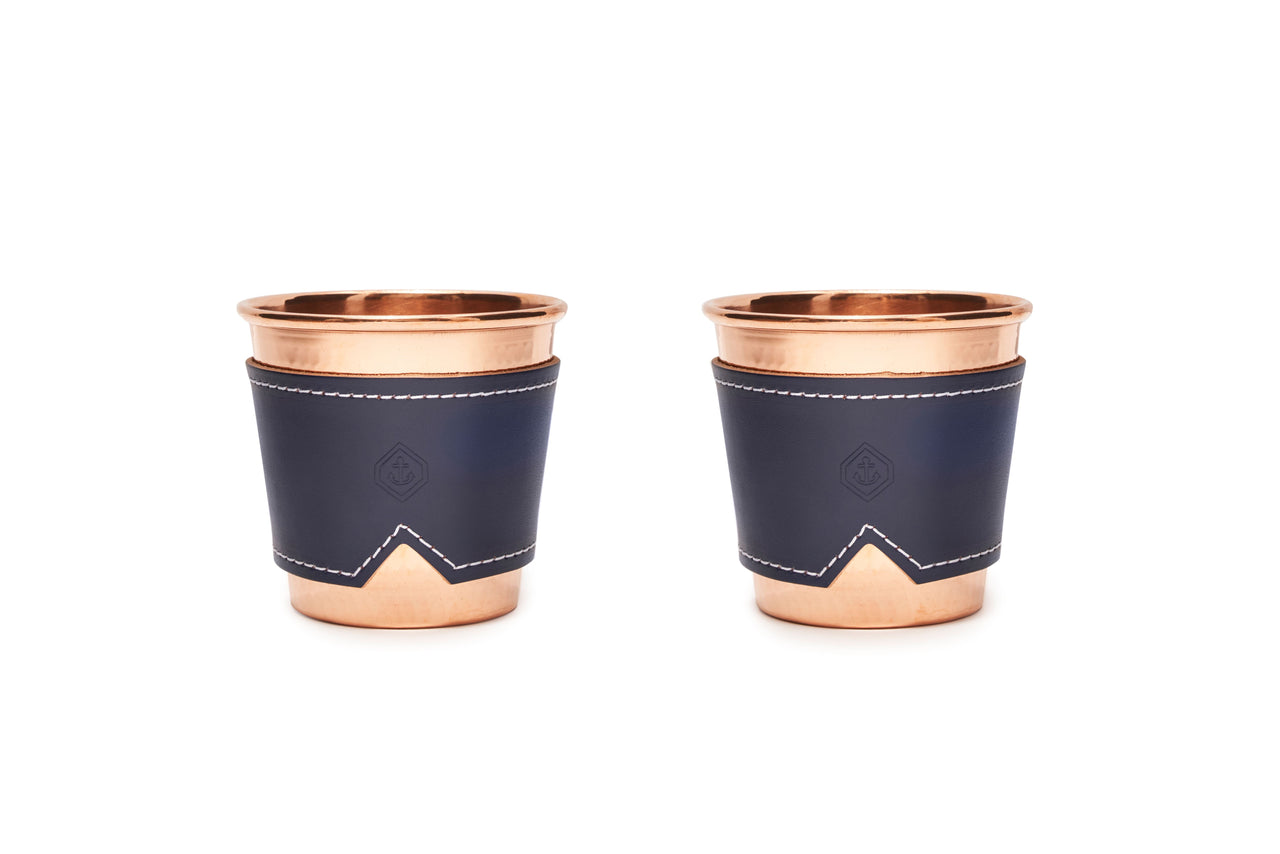 Two 12 oz hammered copper mugs with indigo leather sleeves and white stitching.