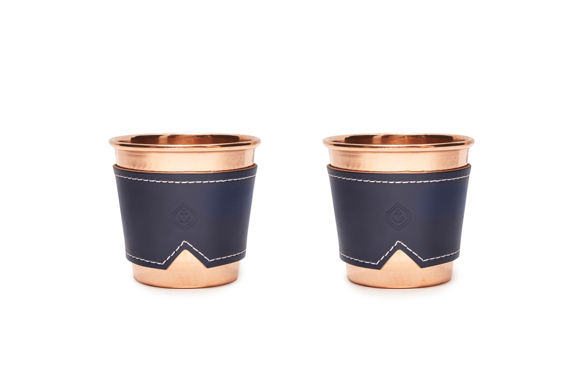 Two 12 oz hammered copper mugs with indigo leather sleeves and white stitching.