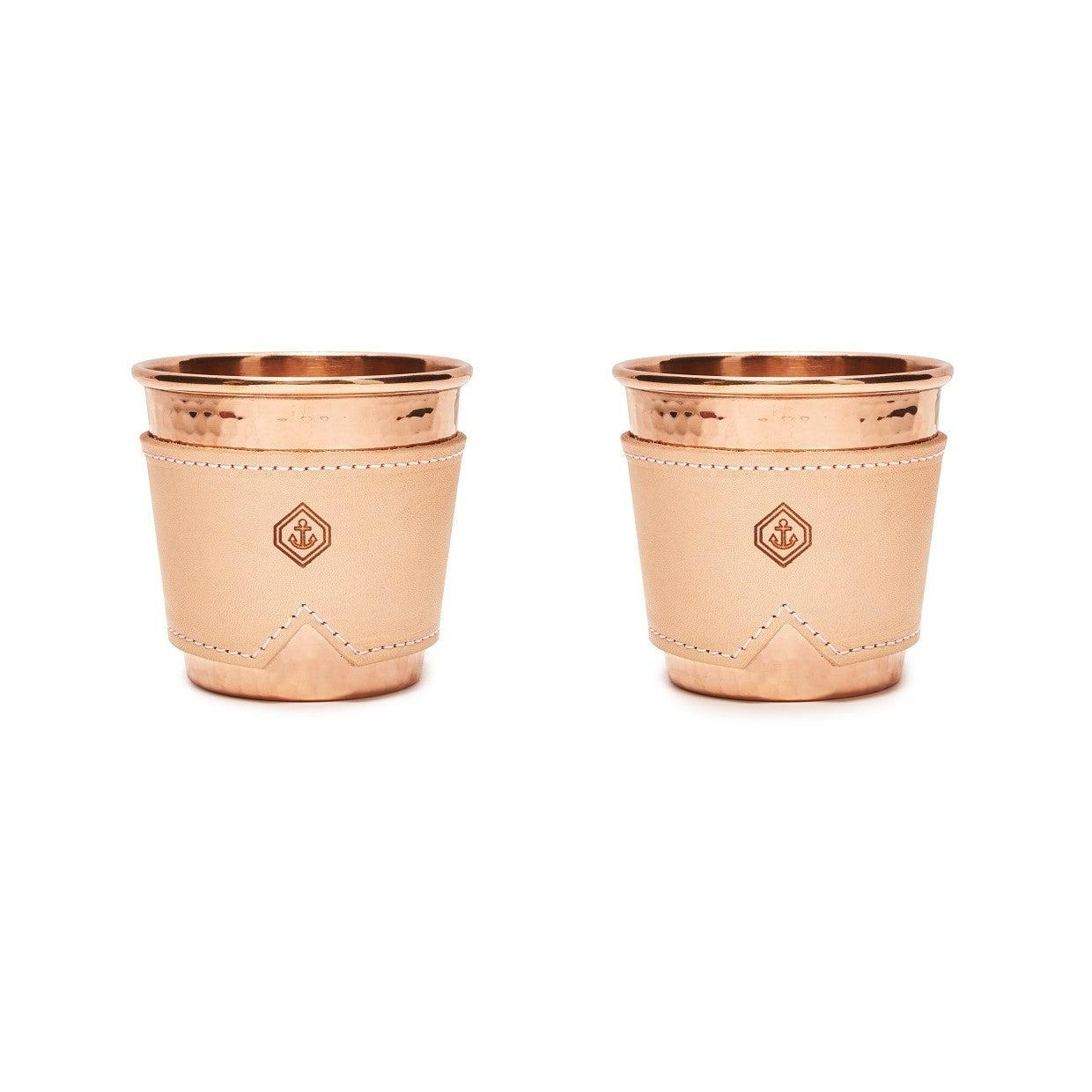 Two 12 oz hammered copper mugs with natural leather sleeves featuring an anchor logo.