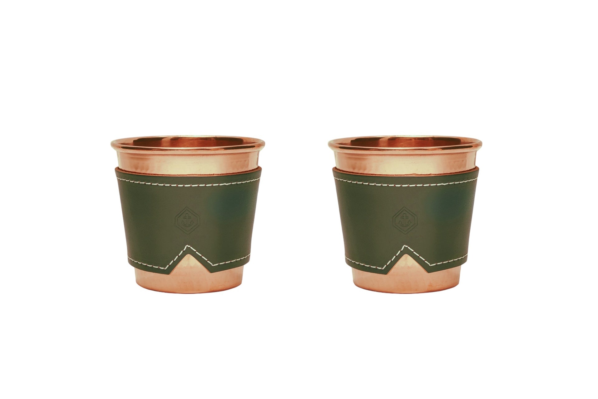 Two 12 oz hammered copper mugs with olive leather sleeves and white stitching.