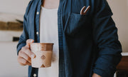 Man in blue shirt holding a hammered copper mug with a natural leather sleeve, showing the brand logo.