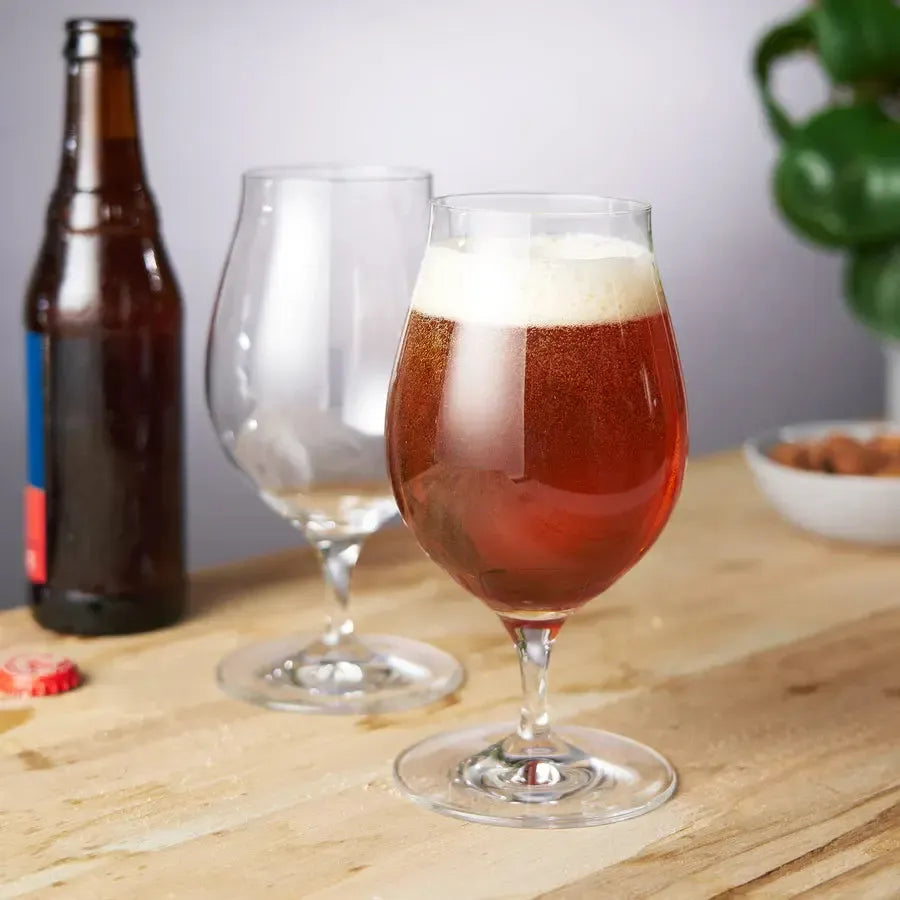Two clear crystal Spiegelau Barrel Aged Beer Glasses, one filled with amber beer, on a wooden surface.