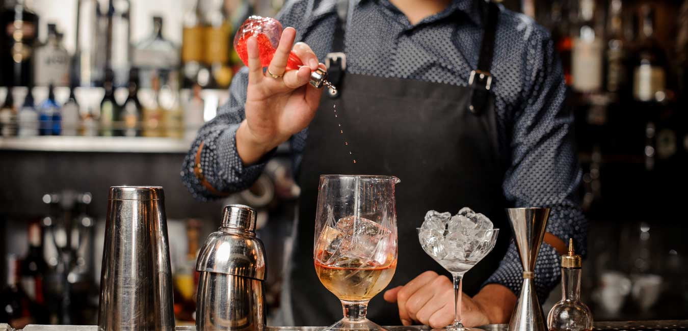 Bartender pouring craft cocktail from stainless shaker into coupe glass