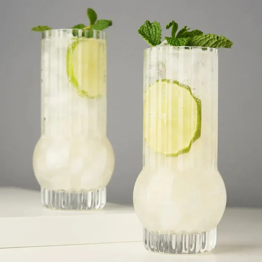 Two clear, ribbed Art Deco crystal highball glasses filled with cocktails, lime, and mint.