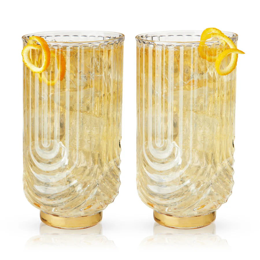 Set of 2 Gatsby highball glasses with gold bases, ribbed clear crystal, and orange peel garnishes.