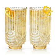 Set of 2 Gatsby highball glasses with gold bases, ribbed clear crystal, and orange peel garnishes.