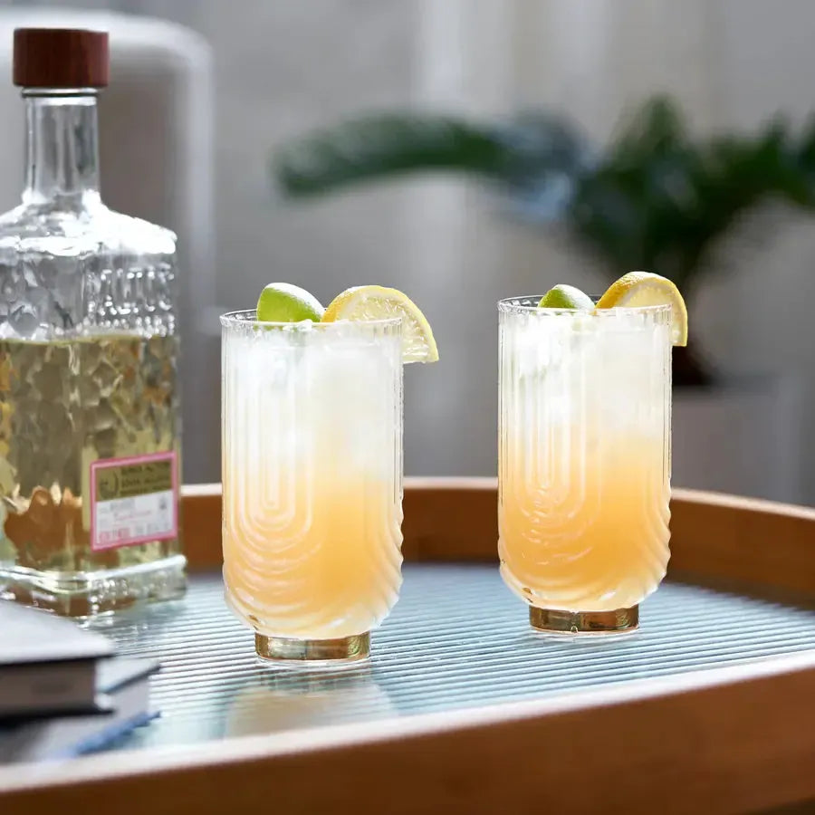 Two Viski Deco Gatsby 15 oz. highball glasses with gold electroplating, filled with cocktails and garnished.