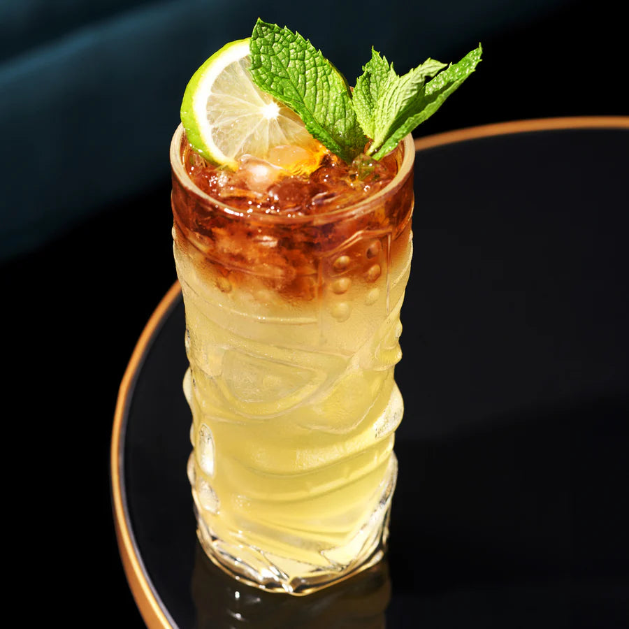 Viski Pacific Crystal Tiki Glass with a layered tropical cocktail, garnished with lime and mint.