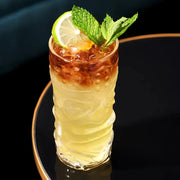 Viski Pacific Crystal Tiki Glass with a layered tropical cocktail, garnished with lime and mint.