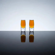 Two clear crystal shot glasses with heavy bases, filled with amber liquid, on a reflective surface.